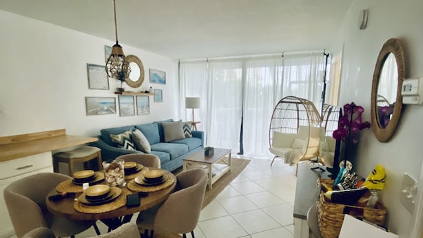 Un salon moderne avec un coin repas, comprenant un canapé, un fauteuil suspendu et une table à manger dressée avec des assiettes et des couverts.