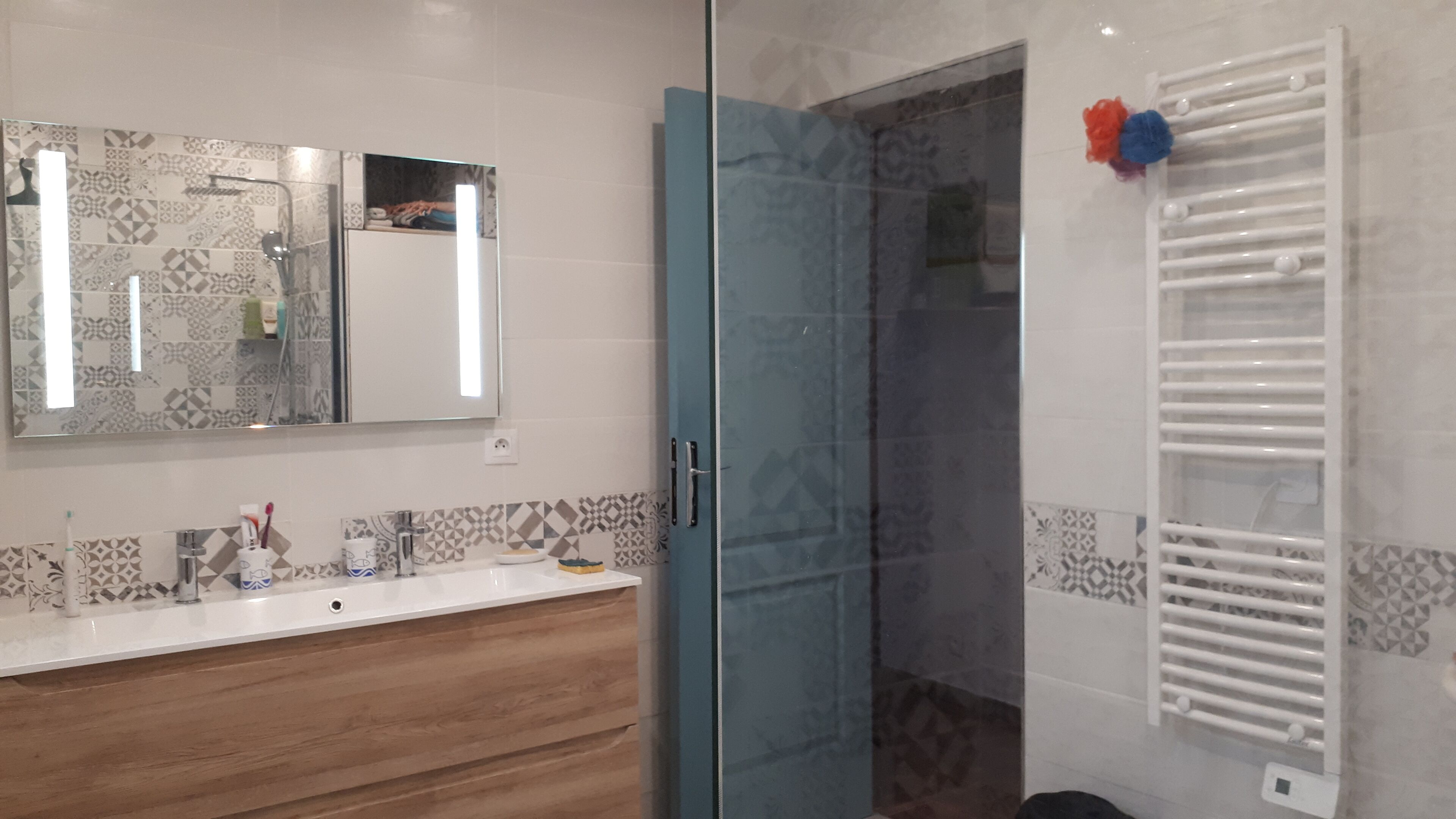 A modern bathroom with a wooden vanity, a large mirror, and a glass shower enclosure.