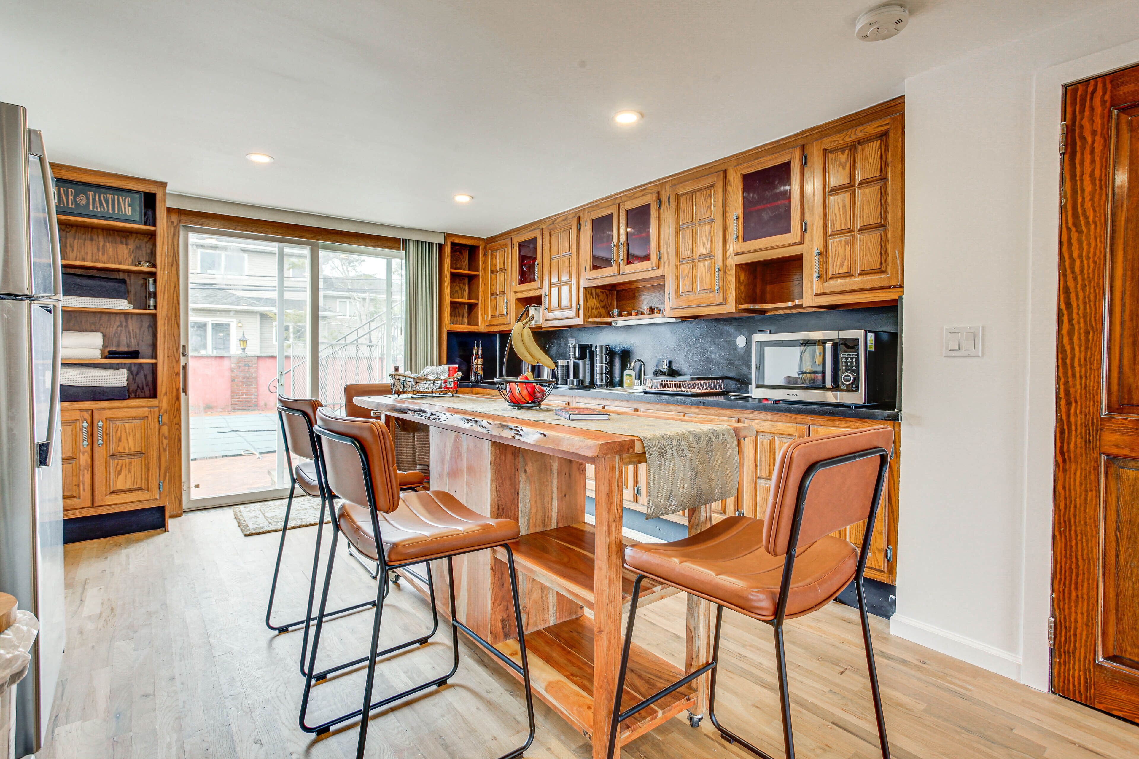 A modern kitchen with wooden cabinets, a central island with stools, and a large window.