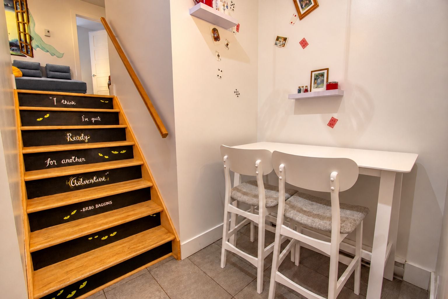 A staircase with motivational phrases, a white desk with two chairs, and wall decorations including playing cards.