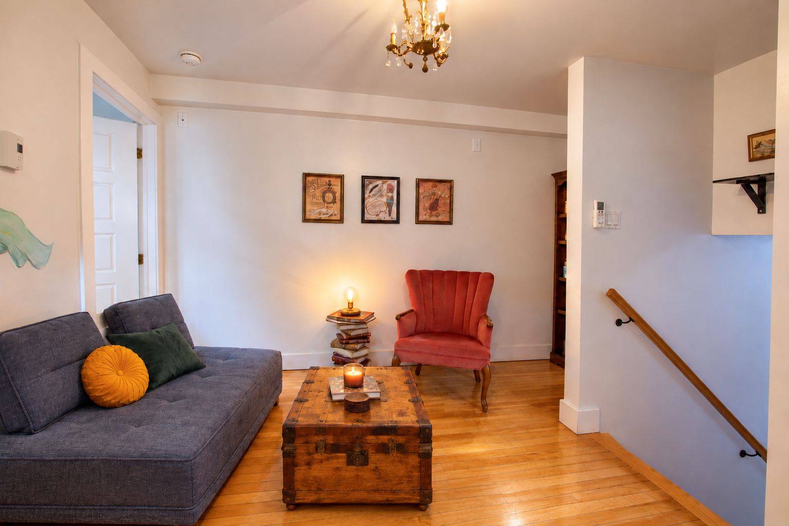 Een woonkamer met een grijze bank, een rode fauteuil, een houten salontafel en een trap.