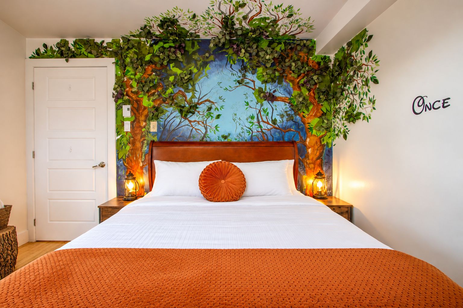 A bedroom with a bed, a wall mural, a door, and a wall sign.