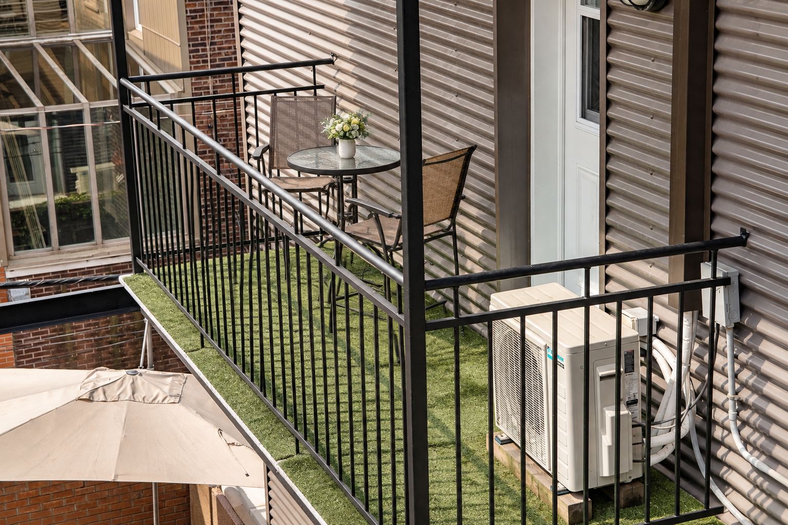 Un balcon avec une petite table et des chaises, un pot de fleurs et un climatiseur blanc.