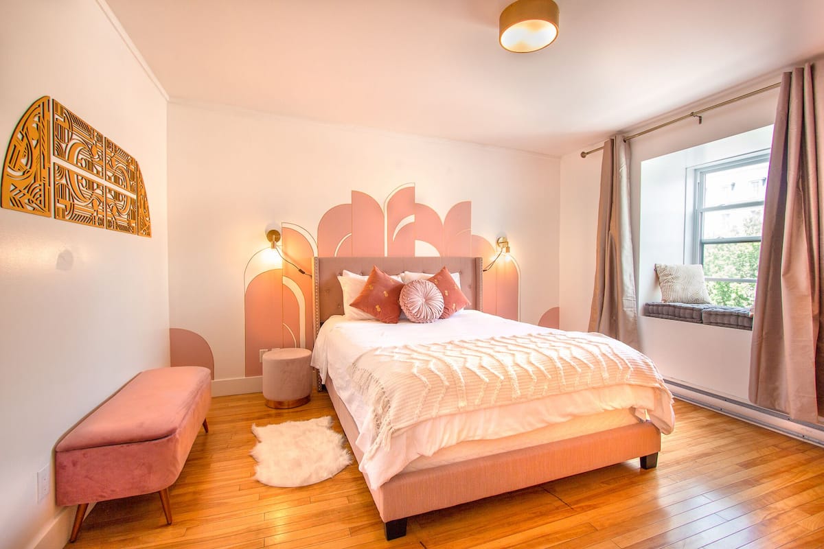 A modern bedroom with a large bed, a bench, a round rug, and a window with curtains.