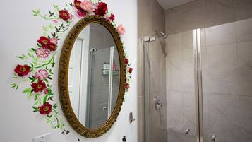 A bathroom with a large oval mirror, a shower, and a wall with floral decorations.