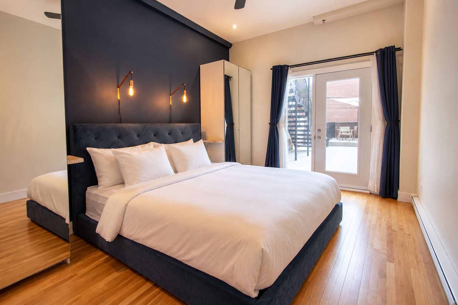 A modern bedroom with a large bed, a dark headboard, and a sliding glass door to the outside.
