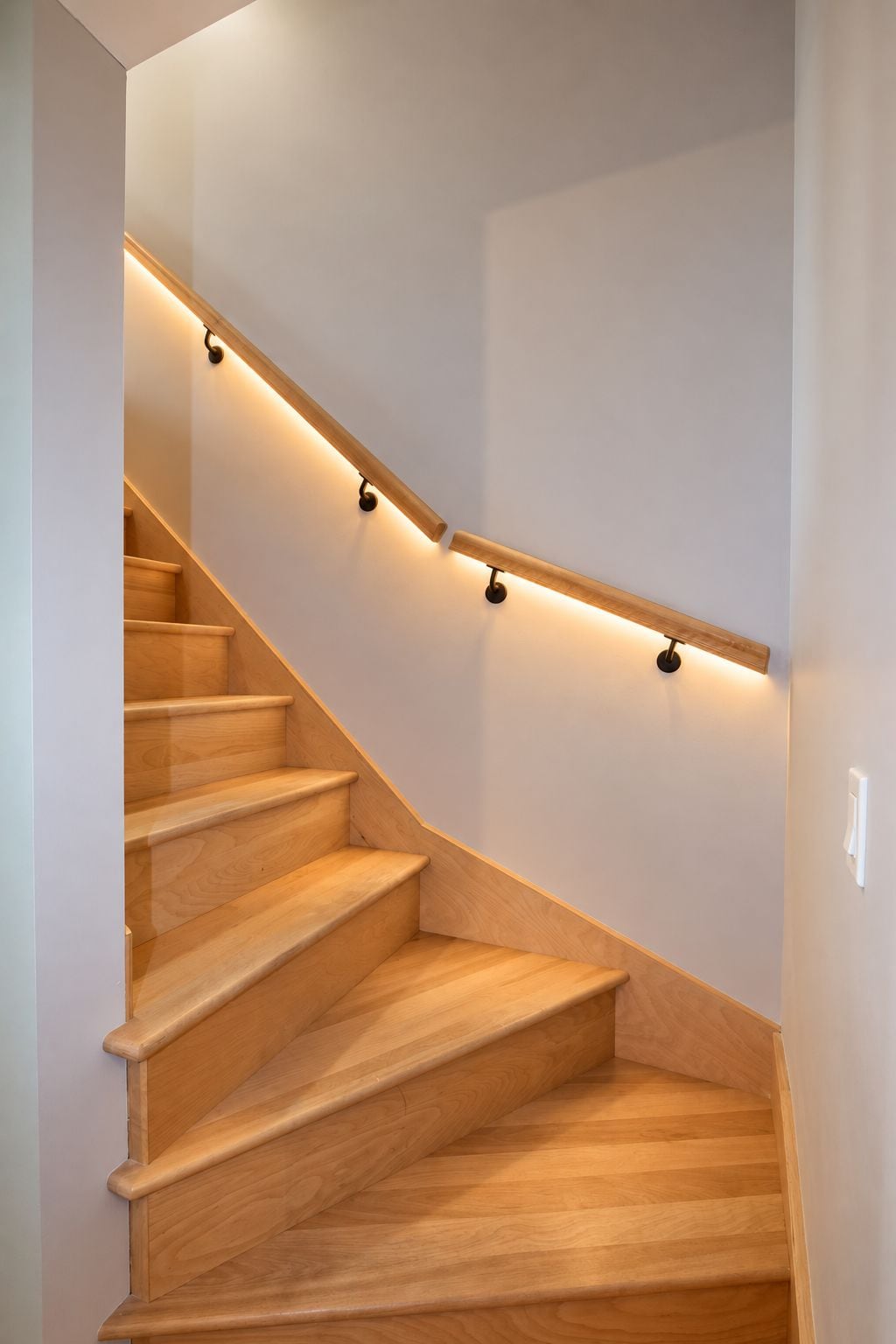 Una scala in legno dalla forma curva con illuminazione a parete.