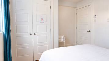 Une chambre d’hôtel avec un lit, deux portes blanches, un porte-serviettes et un thermostat fixé au mur.
