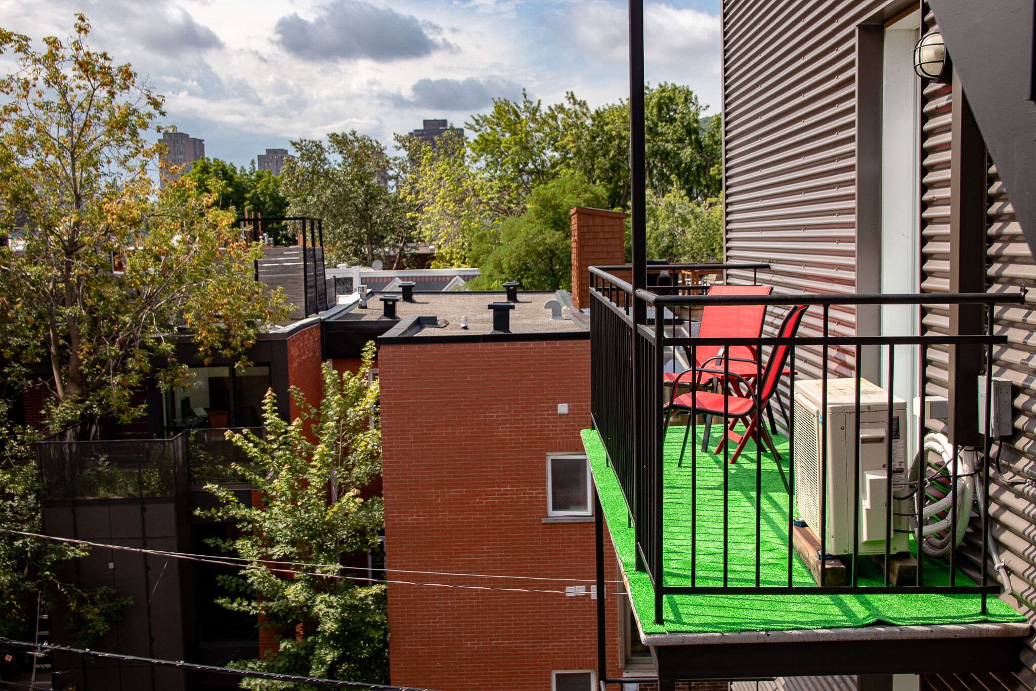 Une terrasse sur le toit, avec une pelouse artificielle verte, une chaise rouge et un appareil de climatisation.