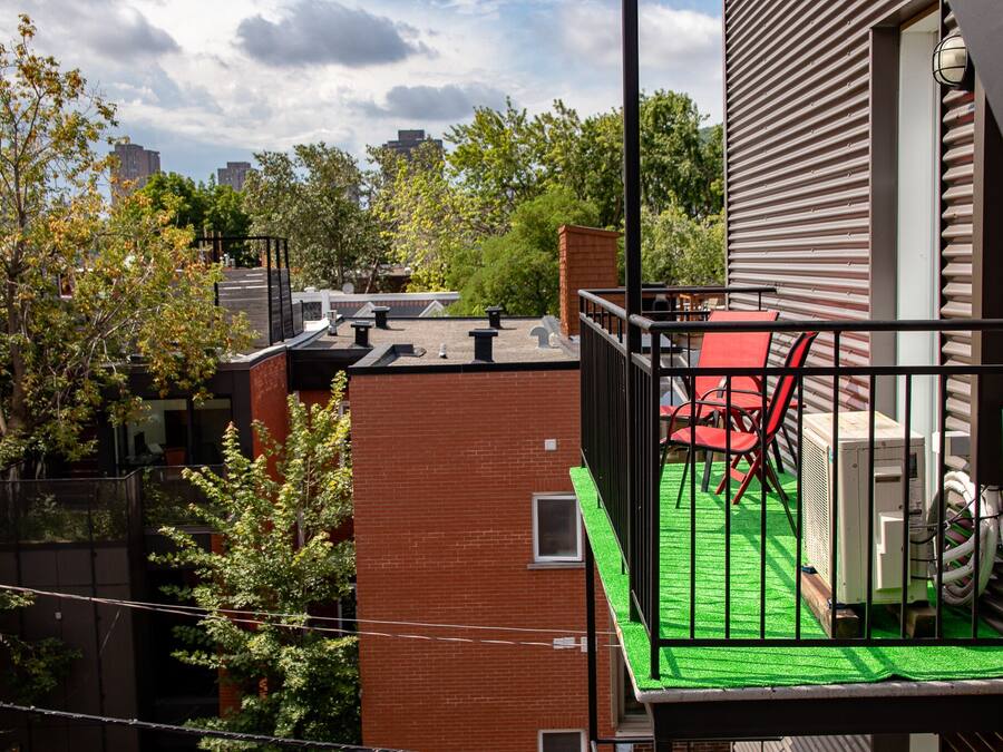 Eine Dachterrasse mit künstlichem Rasen, einem roten Stuhl und einer Klimaanlage.