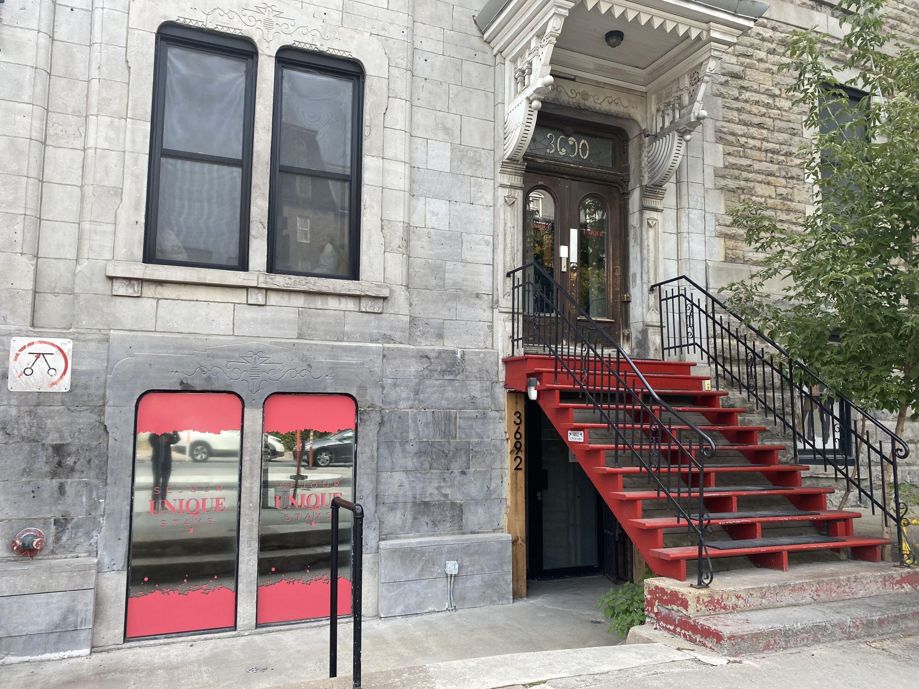 A building with a stone facade, a red staircase, and a sign indicating a no-parking zone.