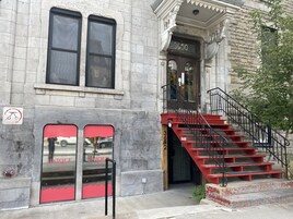 Un immeuble à la façade en pierre, avec un escalier rouge et une signalisation indiquant une zone où le stationnement est interdit.