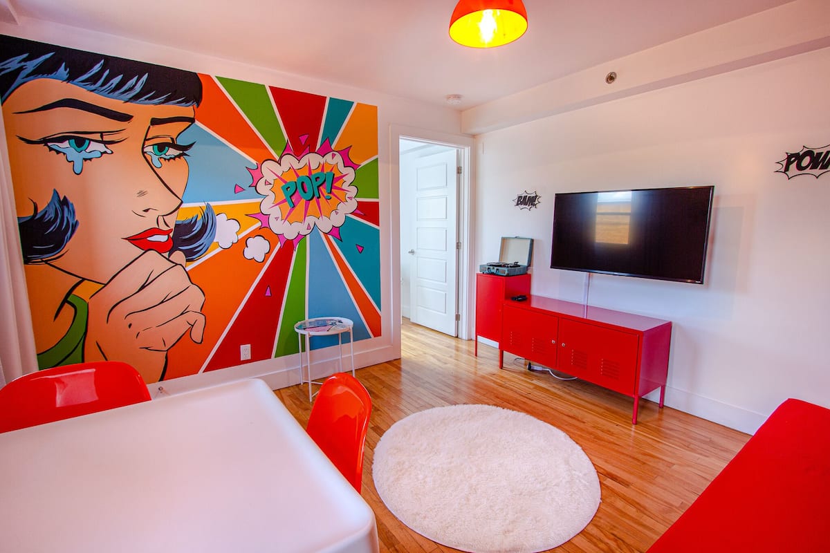 A modern living room with a vibrant pop art mural, a flat-screen TV, and a red cabinet.