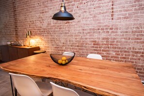 Una mesa de comedor de madera con una lámpara colgante negra, sillas blancas y un frutero.