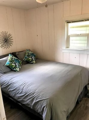 A bedroom with a bed, pillows, a wall clock, and a window.