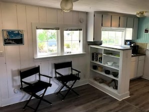 A kitchen with white cabinets, a window with a view, and two black chairs.