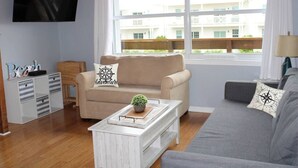 A living room with a beige sofa, a grey sofa, a coffee table, a TV, a window with curtains, and a small wooden cabinet.