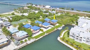 An aerial view of a coastal residential area with houses, a river, and a bridge in the background.