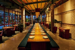 A long dining table with chairs, potted plants, and a view of the ocean. - Desa Potato Head Bali (Keroboken Kelod)