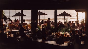 Área de bar ao ar livre com mesas e guarda-sóis, com vista para o oceano.