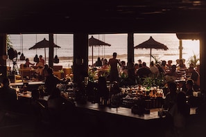 An outdoor bar area with tables and umbrellas, overlooking the ocean. - Desa Potato Head Bali (Keroboken Kelod)