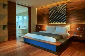 A modern bedroom with a large bed, wooden headboard, and a view of a bathroom. - Desa Potato Head Bali (Keroboken Kelod)