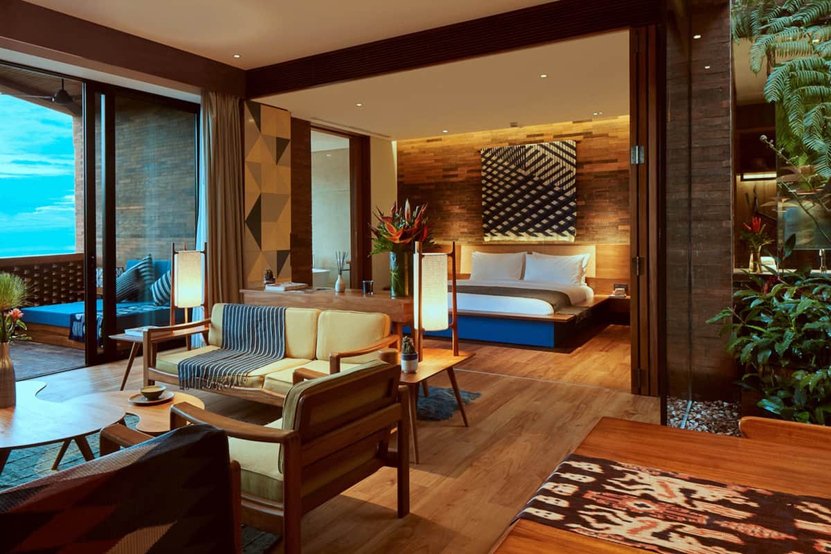 A modern hotel room with a large bed, a sofa, a dining area, and a view of the ocean.