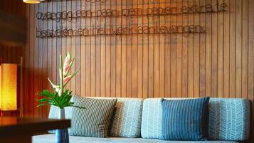 A modern interior with a wooden wall, a sofa with patterned cushions, a round wooden table, and a hanging light fixture.
