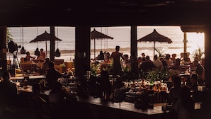 Un espace bar extérieur avec des tables et des parasols, offrant une vue sur l’océan.
