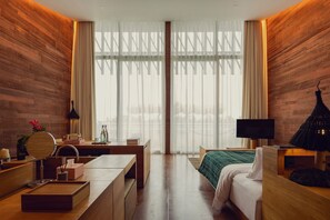 A modern hotel room with a wooden wall, a bed, a desk, a TV, and a large window with curtains.