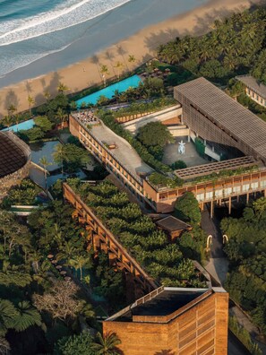 Vue aérienne d’un complexe hôtelier doté d’une piscine, d’une plage et d’une végétation luxuriante.