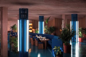A restaurant with blue seating, large blue pillars, and potted plants. - Desa Potato Head Bali (Keroboken Kelod)