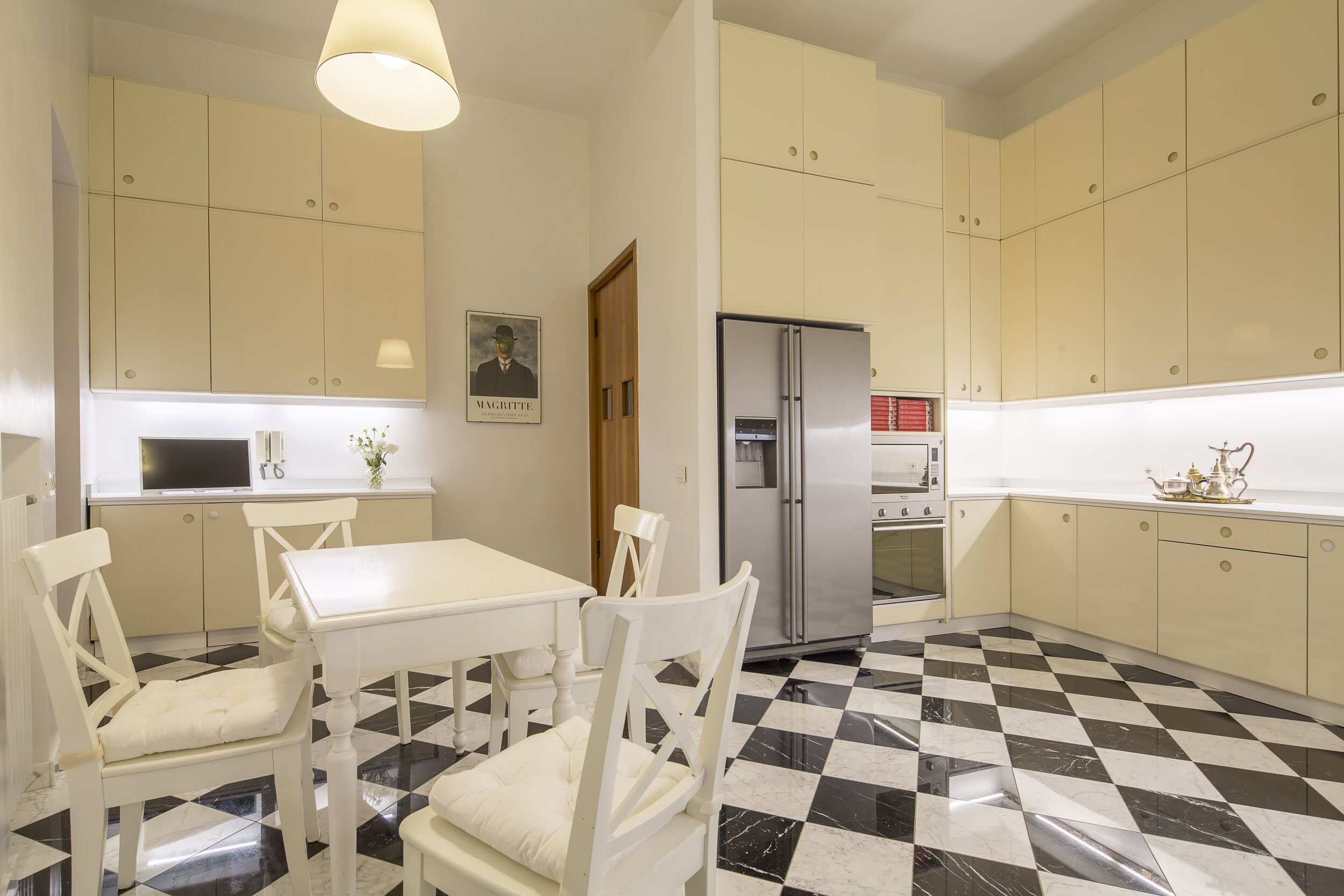A kitchen with a checkered floor, white cabinets, a refrigerator, and a dining table with chairs.
