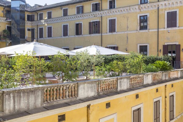 A yellow building with multiple windows and balconies. There are outdoor tables and chairs under white umbrellas.