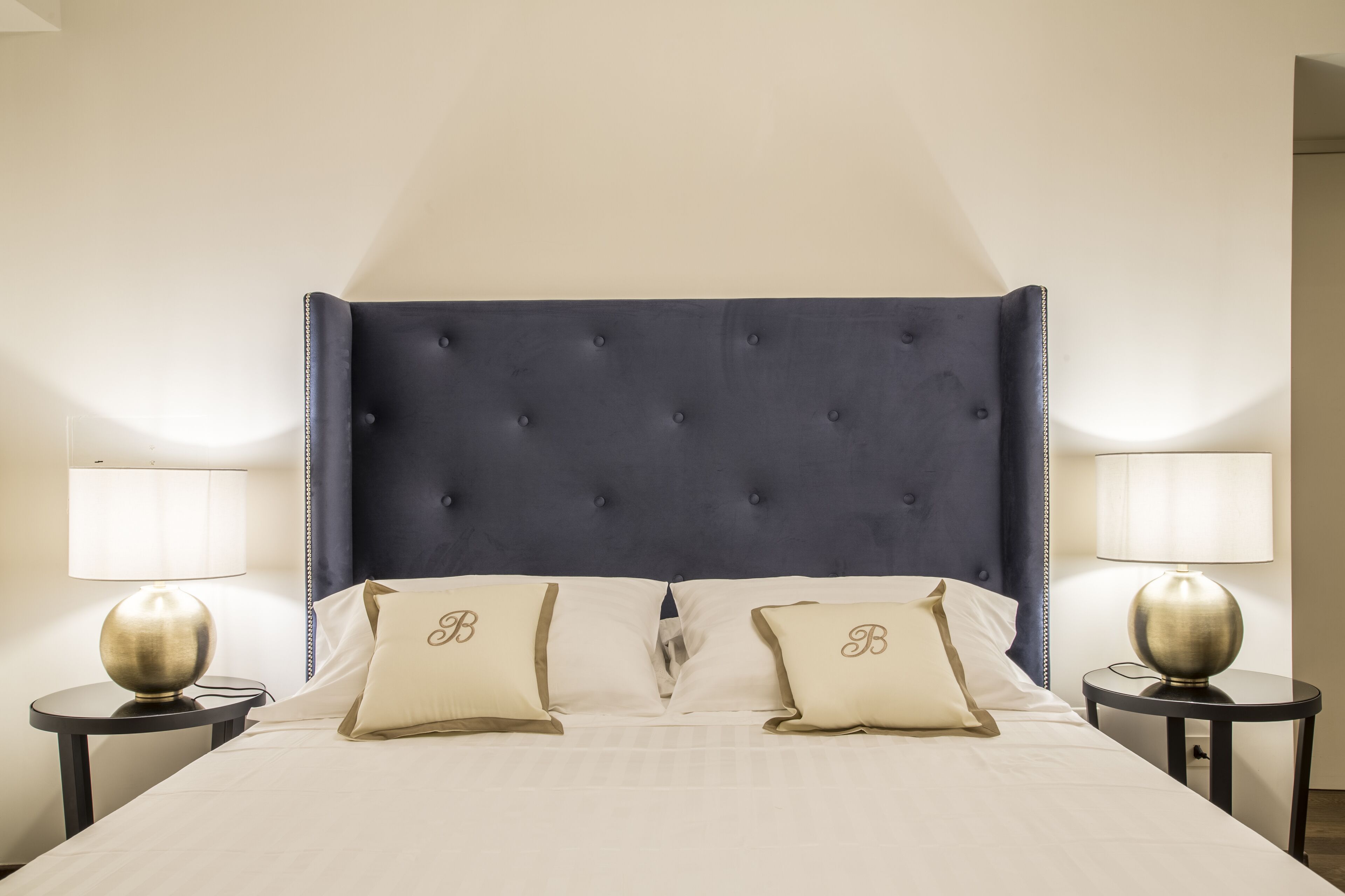 A hotel room with a large bed, two bedside lamps, and a dark blue headboard.