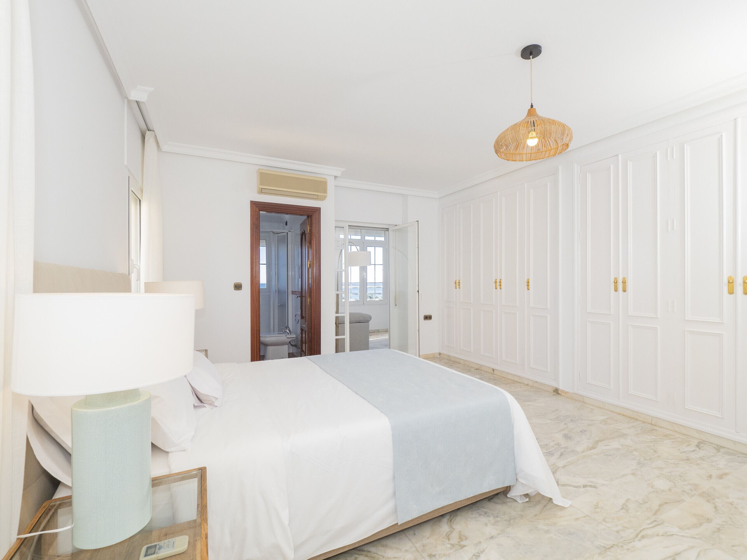A bedroom with a bed, bedside table, lamp, wardrobe, and a hanging light fixture.