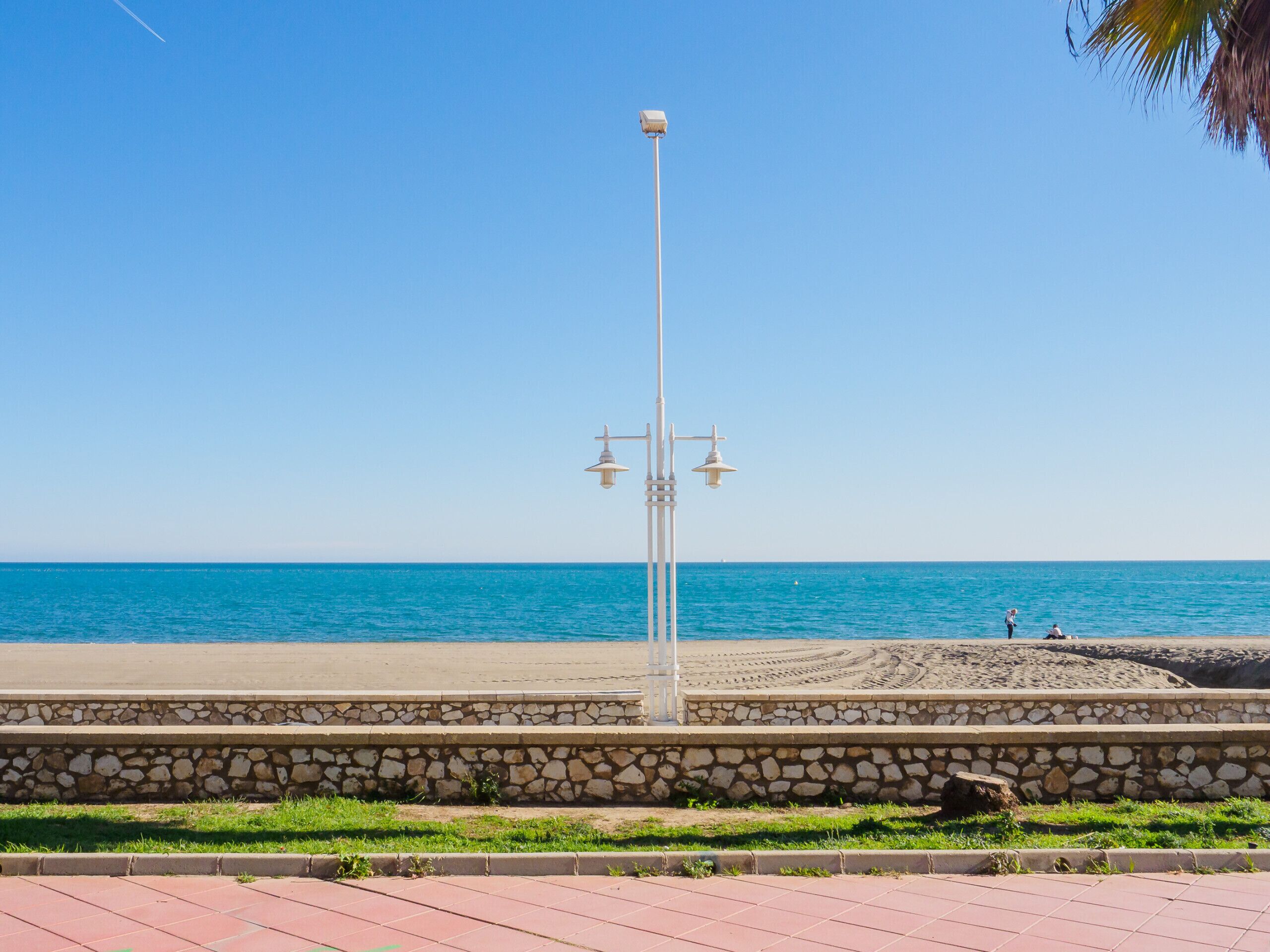 Ein Strand mit einer Steinmauer, einer Laterne und dem Meer im Hintergrund.