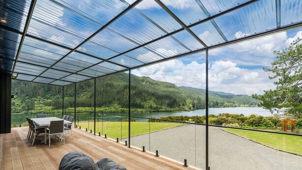 A modern outdoor deck with a glass enclosure, a dining table, chairs, and a seating area. - Lakeview Oasis - Lake Whakamaru Retreat (Mangakino)