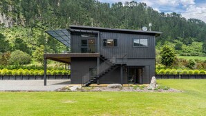 A modern two-story house with a dark exterior, a covered outdoor area, and a staircase leading to the upper floor. - Lakeview Oasis - Lake Whakamaru Retreat (Mangakino)