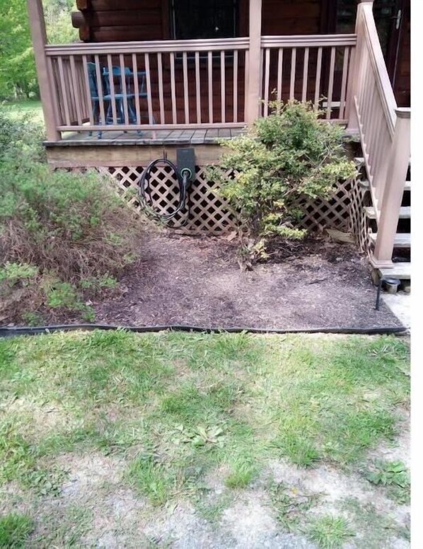 Eine Holzterrasse mit einem Gitterzaun, ein kleiner Gartenbereich mit Mulch und eine Steckdose.