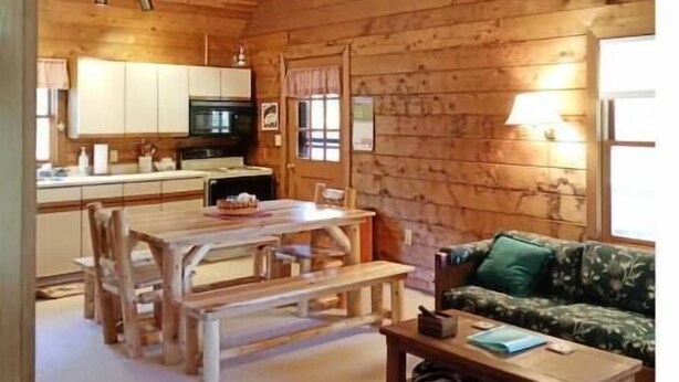 L’intérieur chaleureux d’un chalet comprend une table à manger en bois, des bancs, un canapé et un coin cuisine avec des placards et un réfrigérateur.