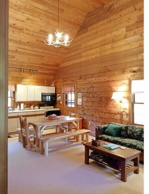 Ein gemütliches Blockhaus-Interieur mit einem Holzesstisch, Bänken, einer Couch und einer Küchenzeile mit Schränken und einem Kühlschrank.