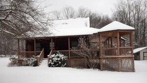 Une cabane en bois dotée d’un porche couvert et d’un toit enneigé, entourée d’arbres.