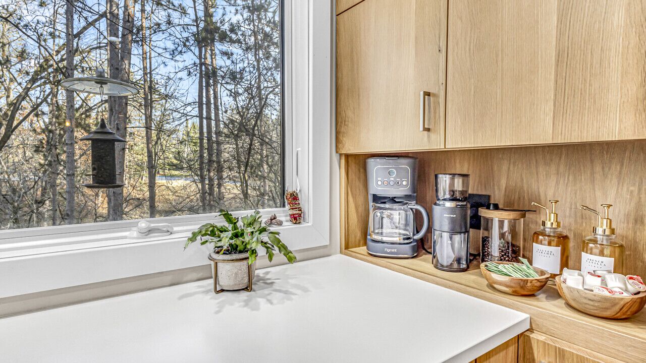 A kitchen with a window view of trees, a coffee maker, a blender, and various kitchen items on the counter.