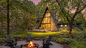 A modern house with a stone chimney, a fire pit with chairs, and a well-maintained garden. - Maple Bluff Escape | A-Frame w/ Theater + Hot Tub (Stevens Point)
