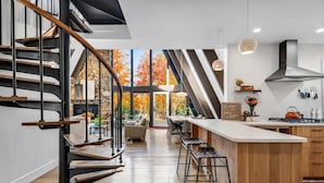 A modern kitchen with a central island, a staircase, and a view of autumn trees. - Maple Bluff Escape | A-Frame w/ Theater + Hot Tub (Stevens Point)
