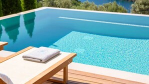 A clear blue infinity pool with wooden loungers and a towel, overlooking a scenic lake and greenery. - 2S Villas Resort - Villa Alpha Α - Private Pool Serenity (SIVOTA)
