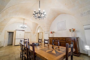 Un comedor con una mesa de madera, sillas, una araña y un adorno de pared.
