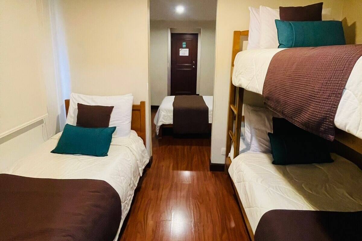 A hotel room with two single beds, a wooden floor, and a door leading to another room.