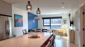 A modern kitchen with a large island, stainless steel appliances, pendant lighting, and a view of the outdoors through large windows. - Cozy Sunset | Amazing views | Private hottub (Revelstoke)